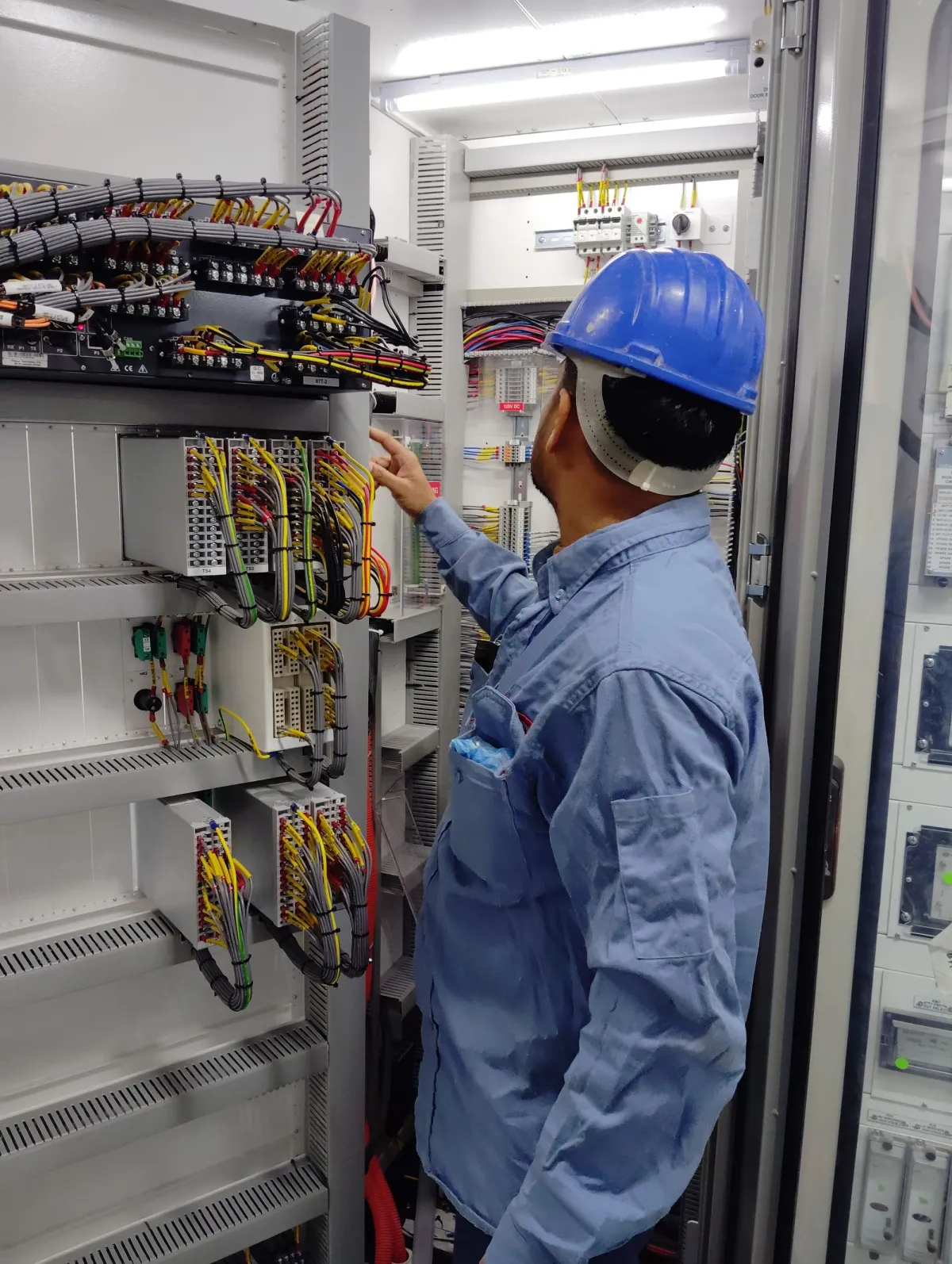 Technicus met veiligheidshelm die de bekabeling van een open schakelkast inspecteert